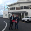 Past Commodore Tony Spencer and Immediate Past Commodore David Seaman hold the burgee in front of Royal New Zealand Yacht Squadron
